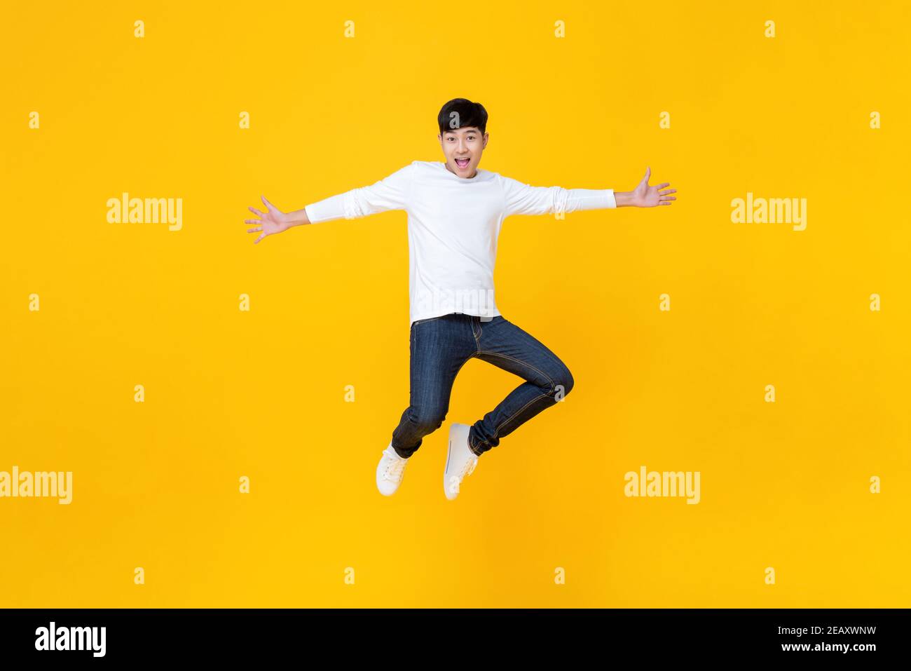 Energetisch glücklich lächelnd junge asiatische Mann in lässigen Kleidung springen Mit ausgestreckten Händen Studioaufnahme isoliert in bunten gelben Hintergrund Stockfoto