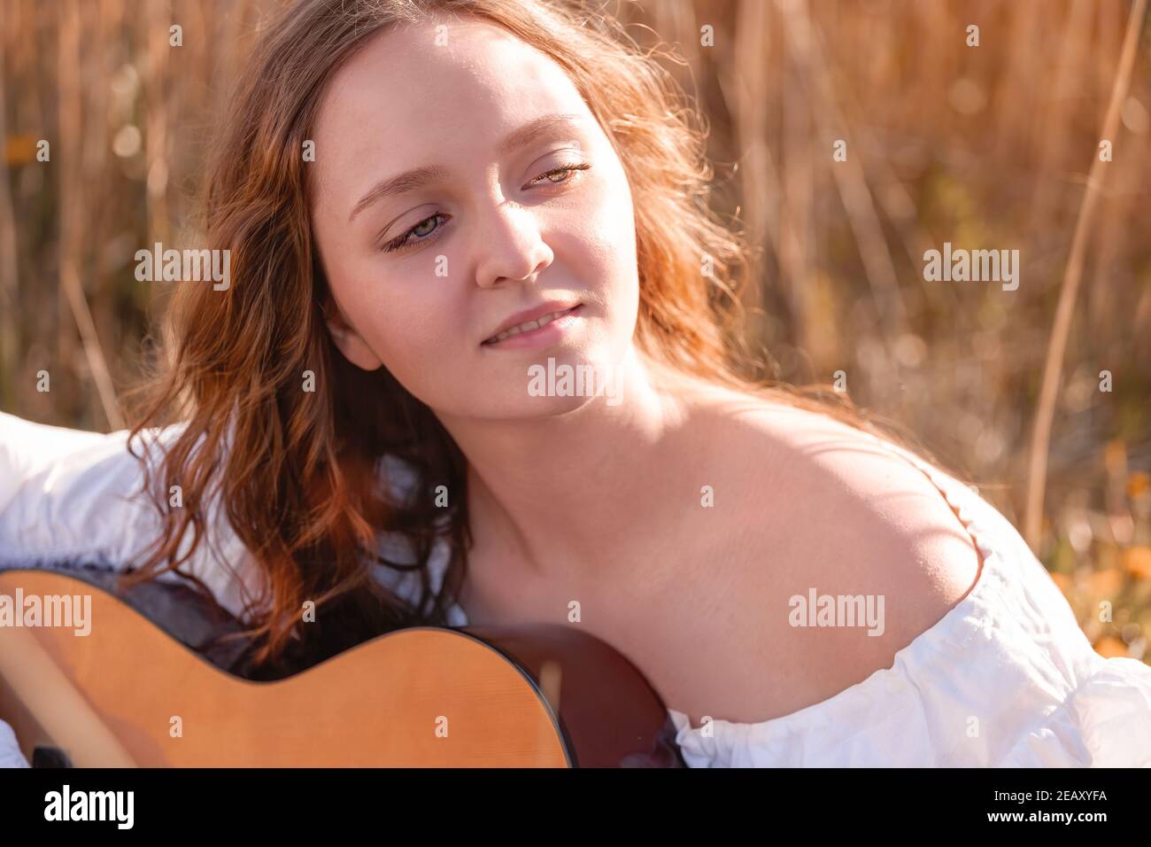 Junge hübsche Frau mit langen Haaren Musiker spielen akustische Gitarre bei Sonnenuntergang Feld im Sonnenlicht. Stockfoto