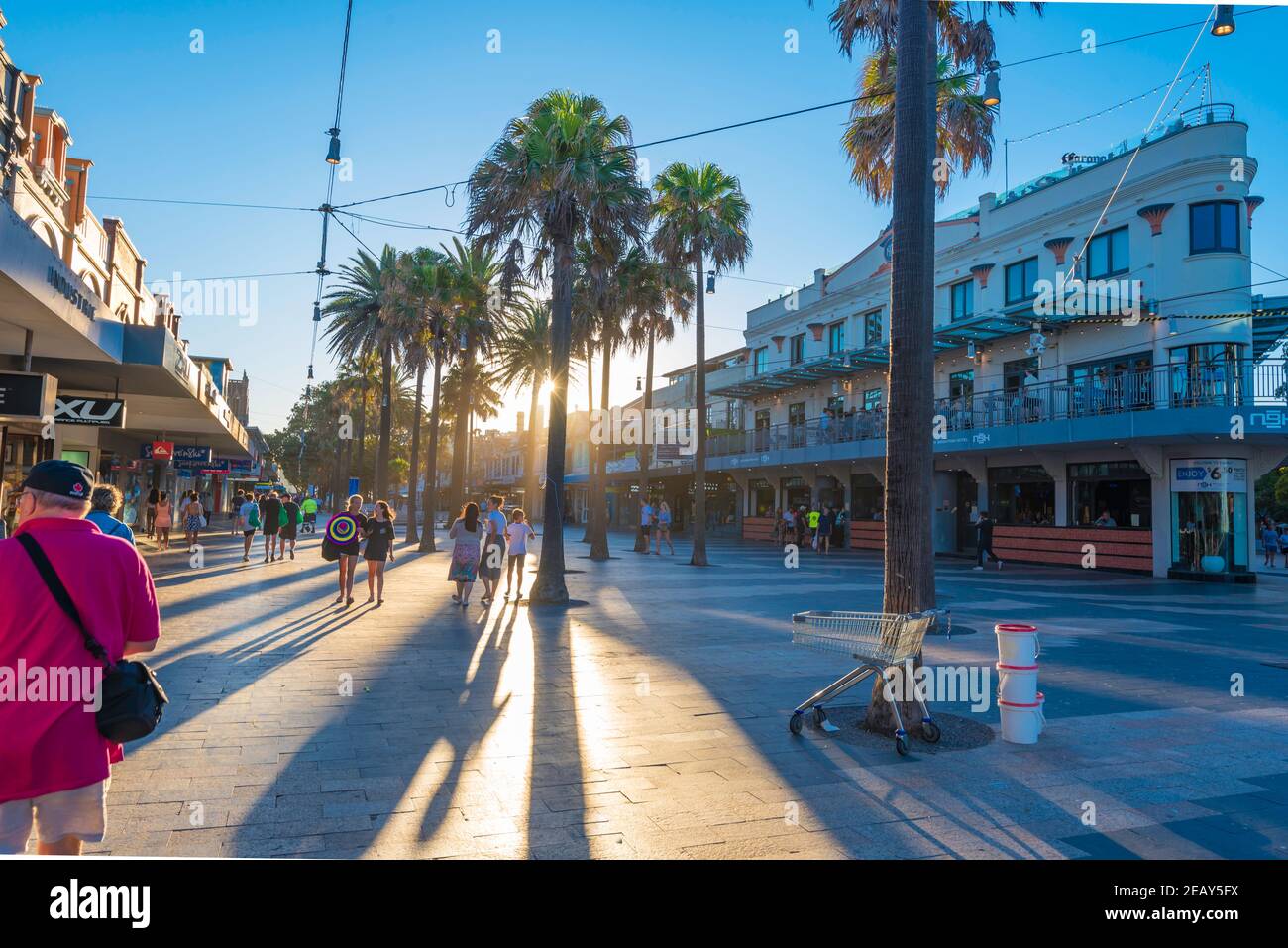 Menschen, die in Richtung der untergehenden Sommersonne entlang des Corso in der Küstenvorstadt von Sydney Manly, New South Wales, Australien, wandern Stockfoto
