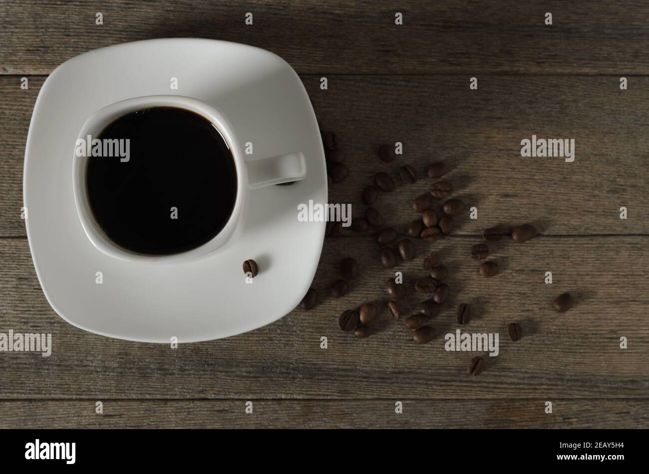Eine Tasse Kaffee auf einem Holztisch mit verstreuten gerösteten Bohnen. Selektiver Fokus. Stockfoto