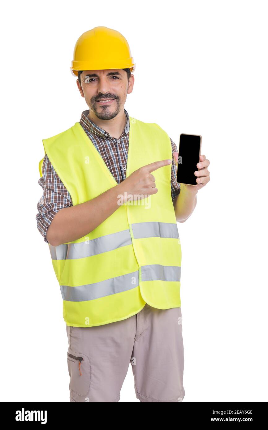Begeistert männlichen Baumeister in Uniform stehen auf weißem Hintergrund und Zeigt auf den Bildschirm des Mobiltelefons, während die Kamera betrachtet wird Stockfoto