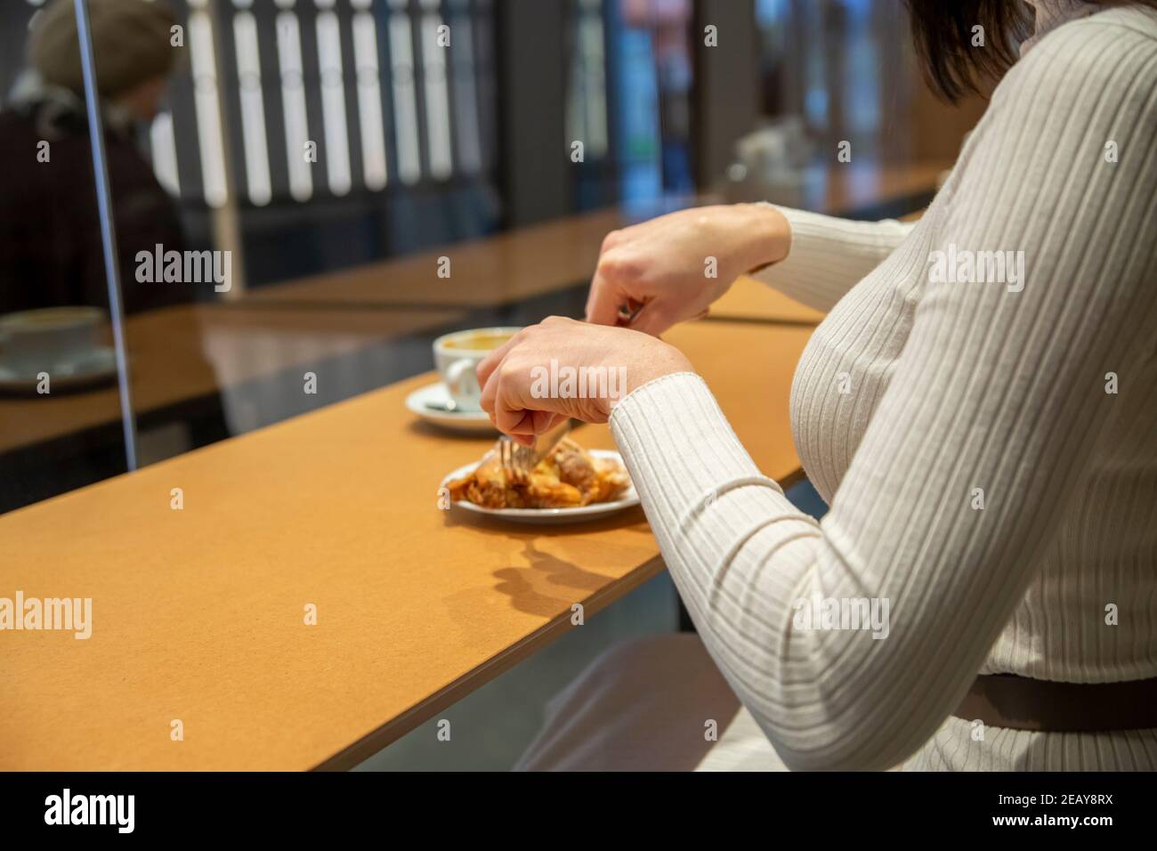 Frau schneidet Croissant und trinkt Kaffee an einem Tisch in einem Café. Kein Gesicht Stockfoto