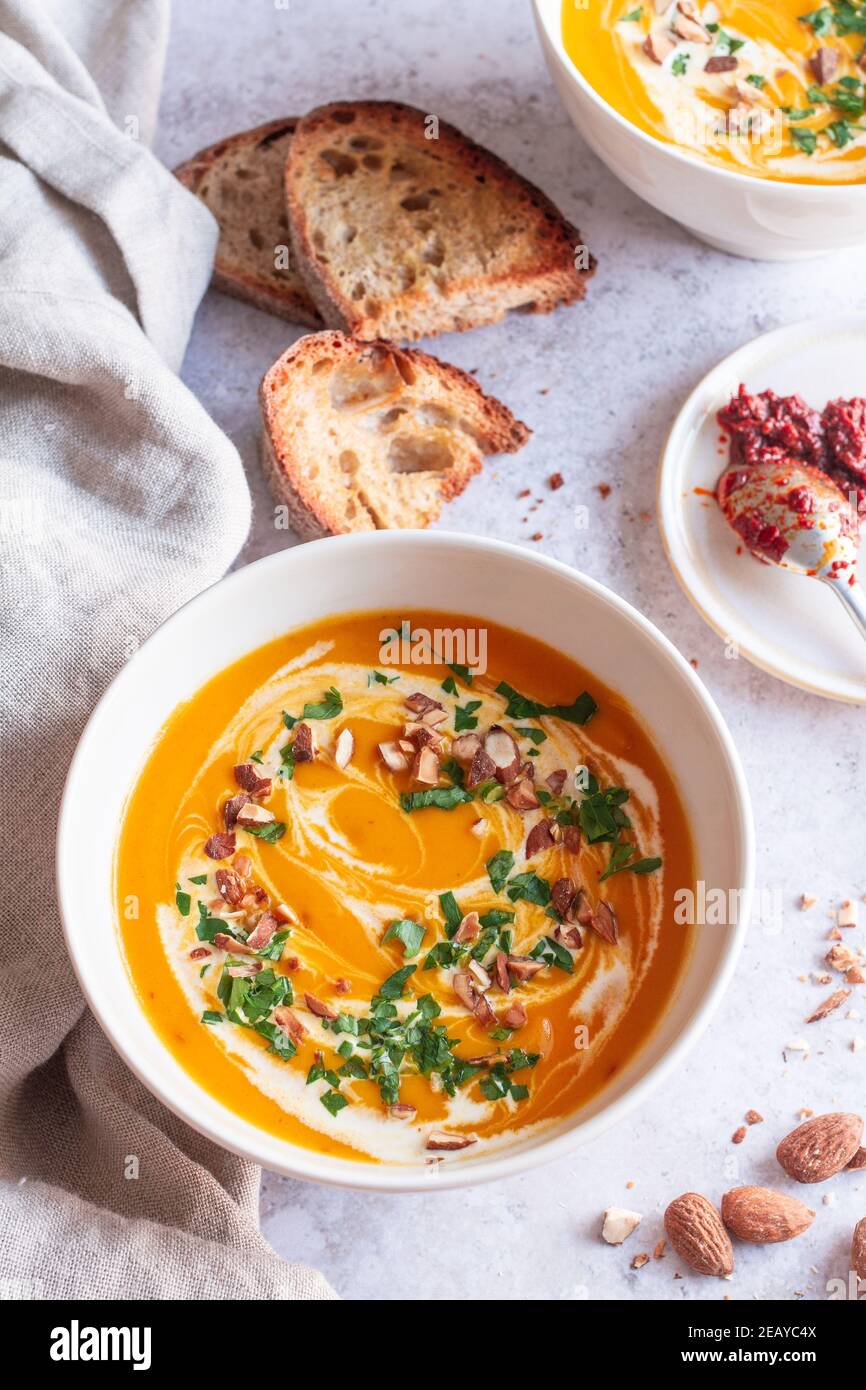 Zwei Schüsseln gewürzte Harissa-Karottensuppe mit beträufelter Sahne, gehackter Petersilie, gehackten Mandeln und geröstetem Brot. Stockfoto
