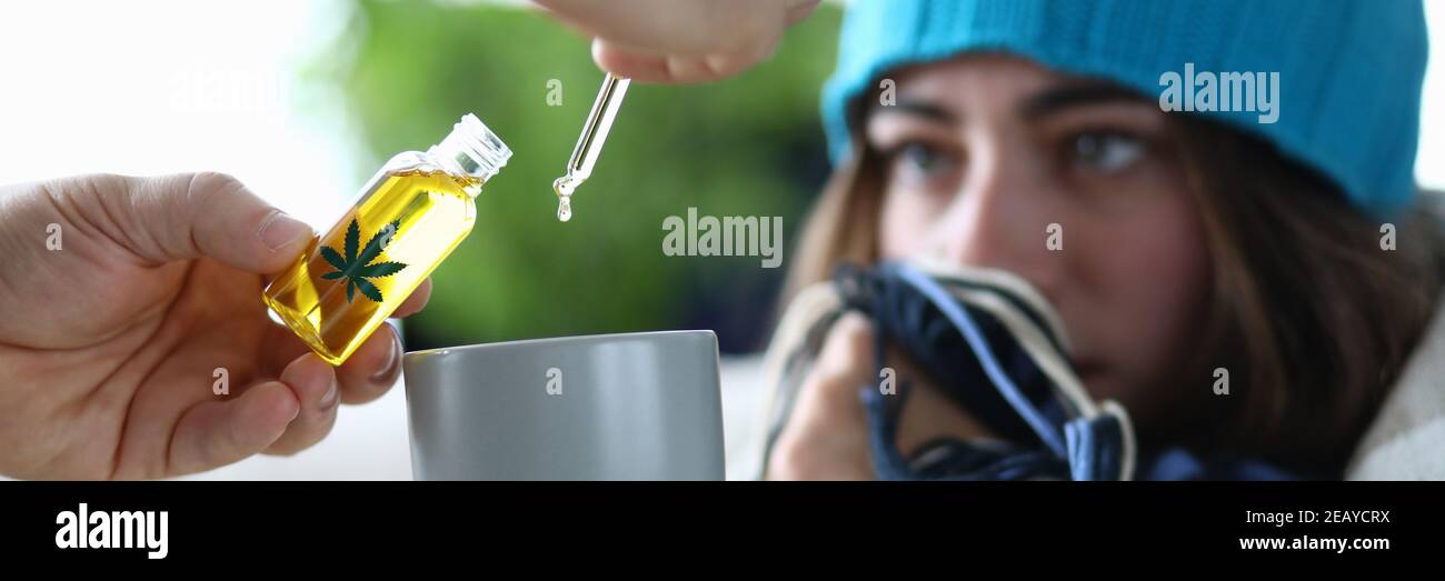 Yung Frau krank mit Grippe tropft in Tasse mit Tropfen Marihuanaextrakt aus der Nähe Stockfoto