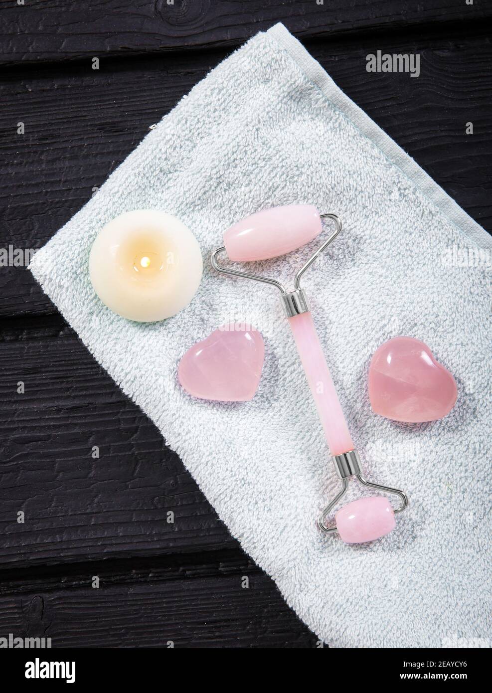 Gesichts rollende Massage-Tool für den Heimgebrauch Gesichtsmassage. Aus kühlenden Rosenquarz Halbedelstein. Flache Sicht auf Holztablett, kühl schwarz rau. Stockfoto