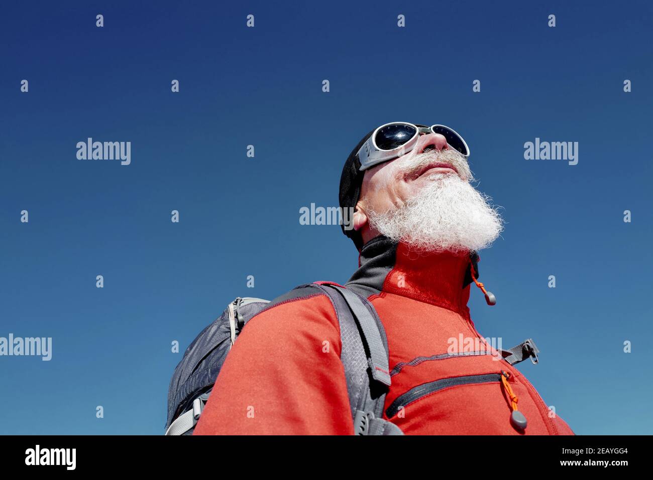 Portrait des Kletterers mit langem weißen Bart in roter Jacke Gegen blau klaren Himmel in den Bergen Stockfoto