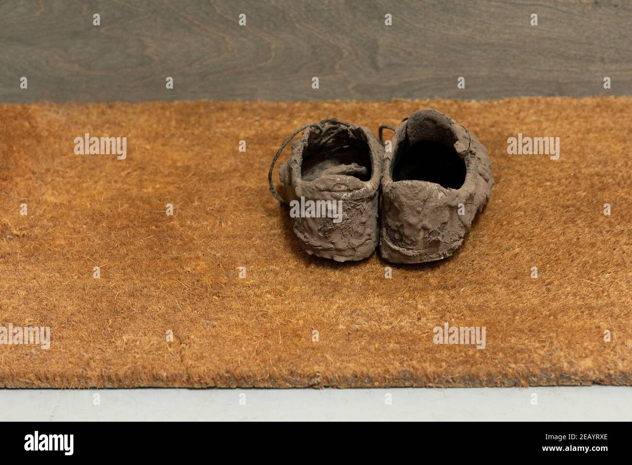 Schmutzige, getrocknete schlammige und unordentliche Sneaker-Schuhe, mit denen sie total bedeckt sind Schlamm, der unerkennbar aussieht, während er auf einer braunen Coco-Fußmatte liegt Stockfoto