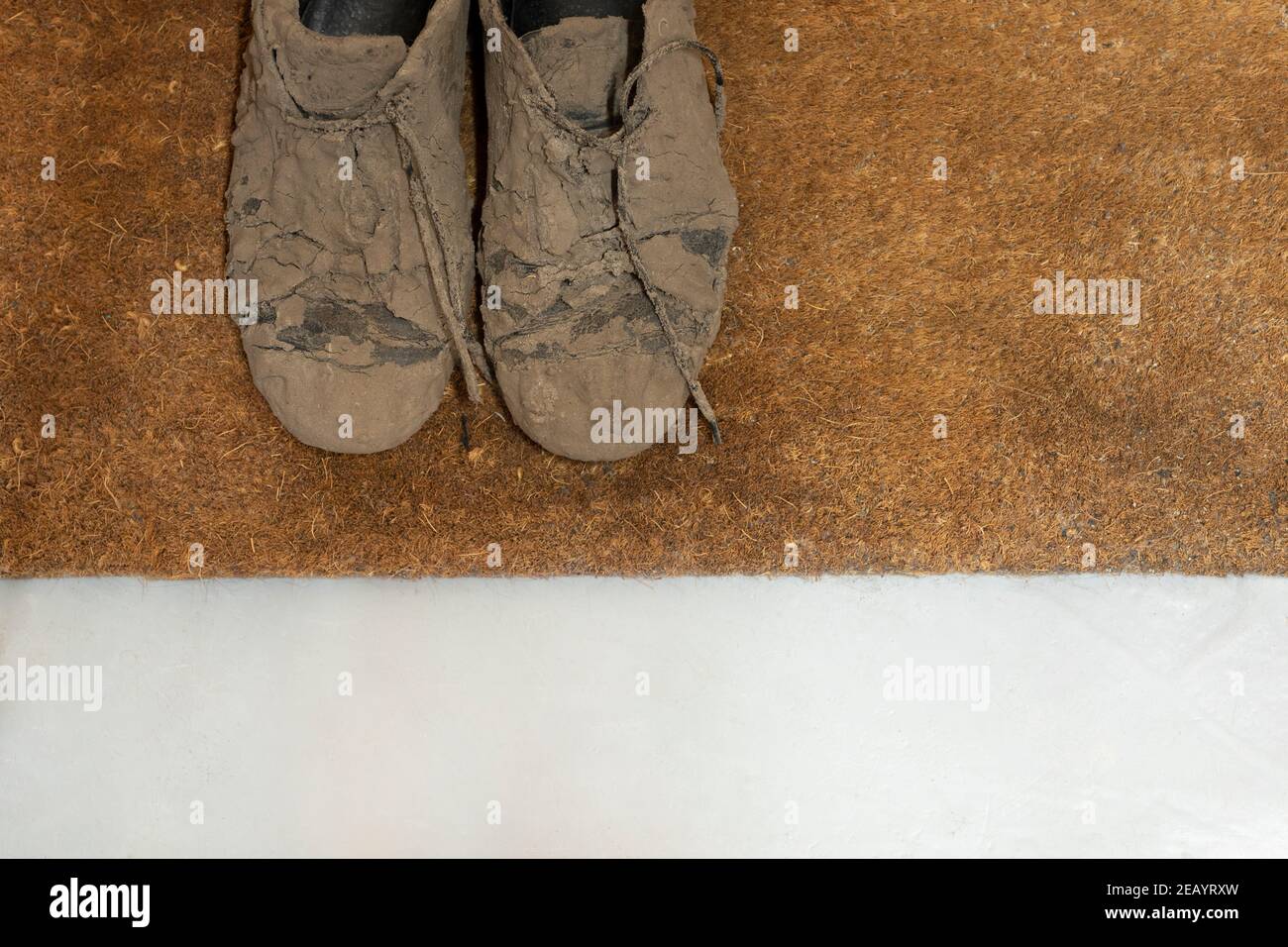 Detailaufnahme von schmutzigen, getrockneten schlammigen und unordentlichen Sneakerschuhen Völlig mit Schlamm bedeckt, der unerkennbar aussieht, während er auf einem liegt Braune Coco-Fußmatte Stockfoto