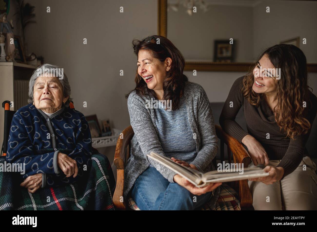 Frauen Generation mit alten kranken Großmutter im Rollstuhl sitzen und lächelnde Tochter und Enkelin suchen ein Fotoalbum. Stockfoto