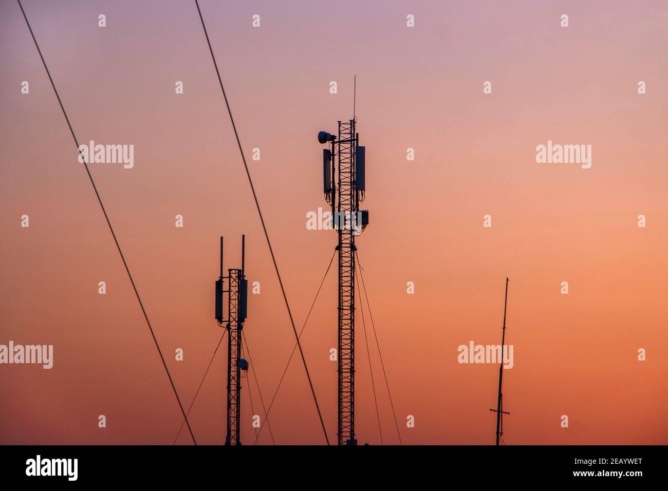 Turm mit einem mobilen Signalsender auf dem Hintergrund eines orangefarbenen wolkenlosen Himmels am Morgen. Stockfoto
