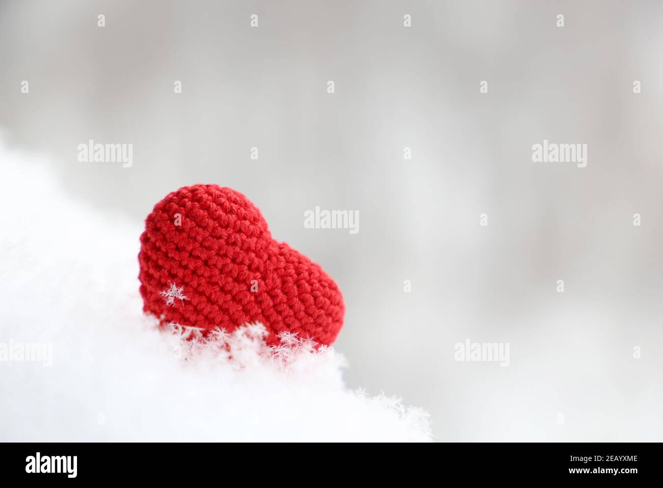 Valentine Herz im Schnee, Hintergrund für den Winterurlaub mit verschwommenem Kopierraum. Rot gestricktes Symbol der romantischen Liebe mit Schneeflocke Stockfoto