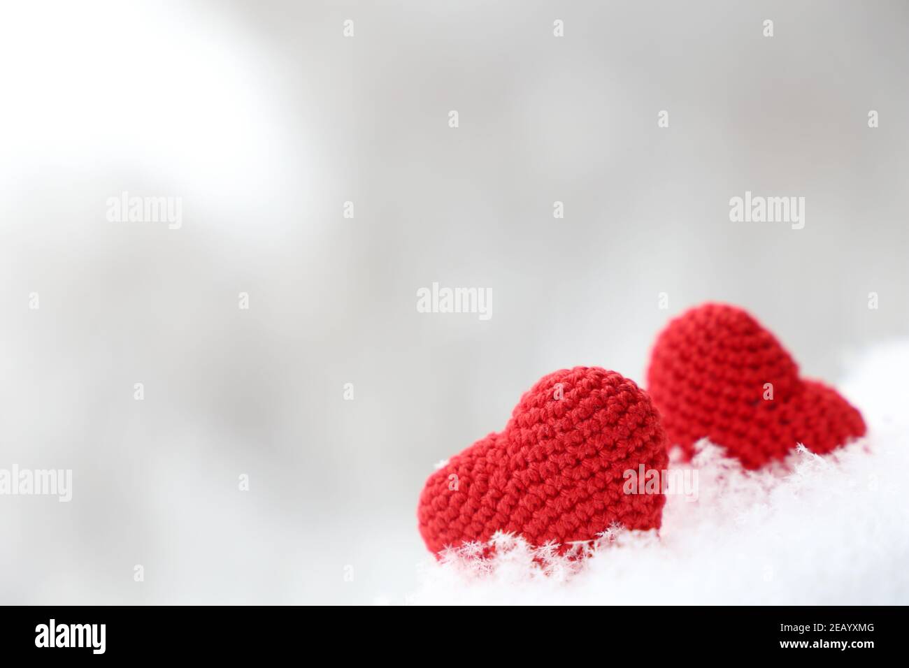 Valentine Herzen im Schnee, Hintergrund für den Winterurlaub mit verschwommenem Kopierraum. Zwei rote gestrickte Symbole der romantischen Liebe Stockfoto