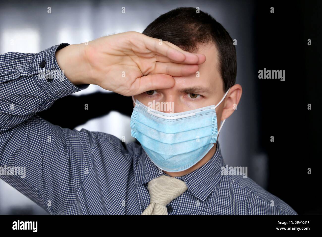 Coronavirus und Fieber Symptome, Mann in Gesichtsmaske und Bürokleidung legte seine Hand auf die Stirn. Kranker Büroangestellter, Konzept der Kopfschmerzen Stockfoto