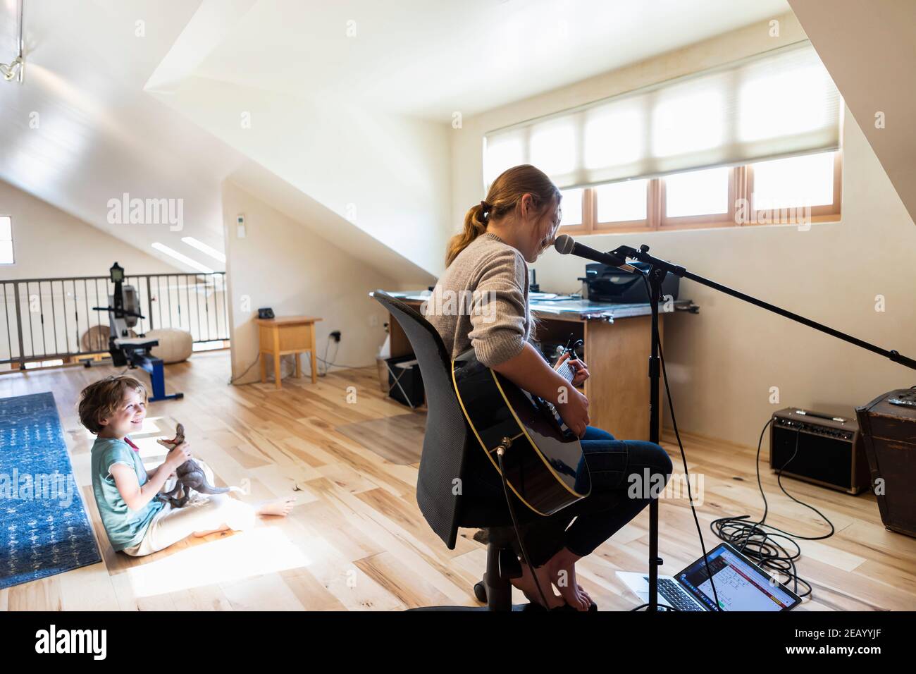 14 Jahre altes Teenager-Mädchen, das Gitarre spielt und singt, ihr Bruder spielt im Hintergrund Stockfoto