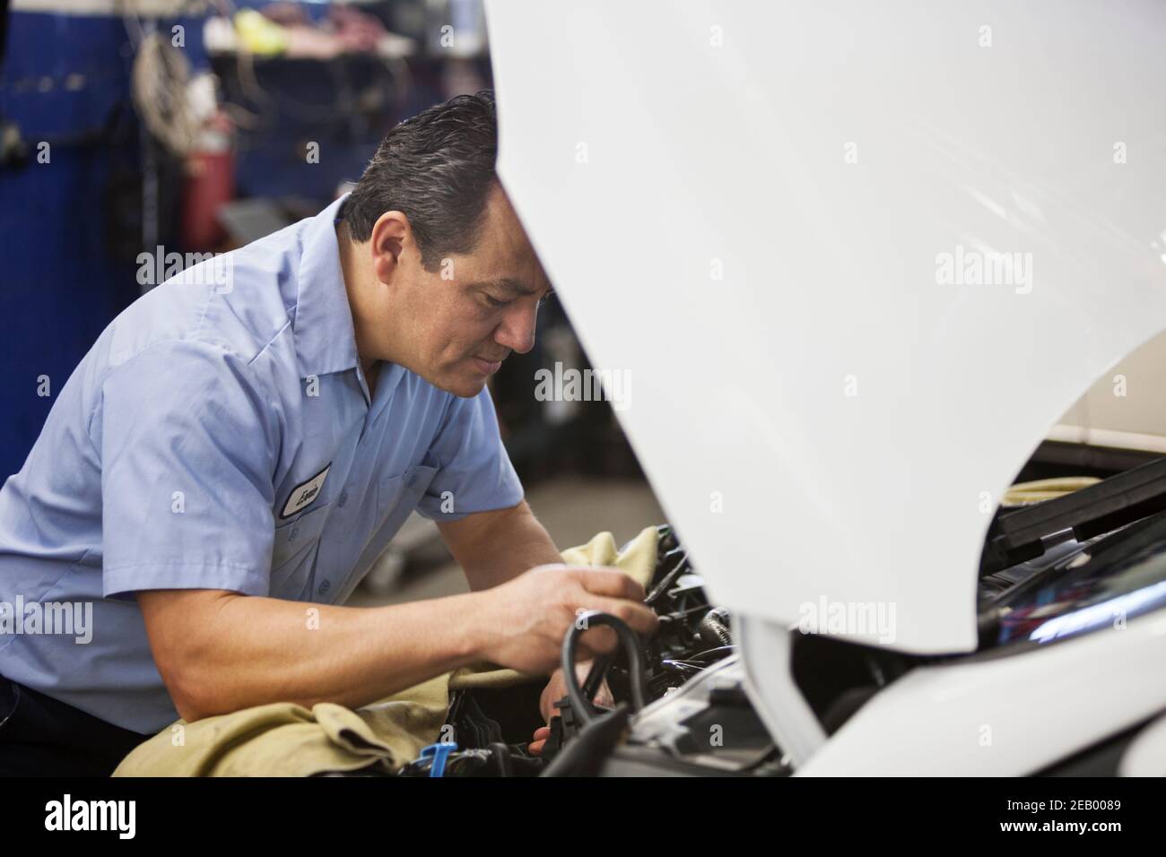 Hispanic Mechaniker stützt sich auf ein Auto, das am Motor arbeitet Fach in einer Autowerkstatt Stockfoto