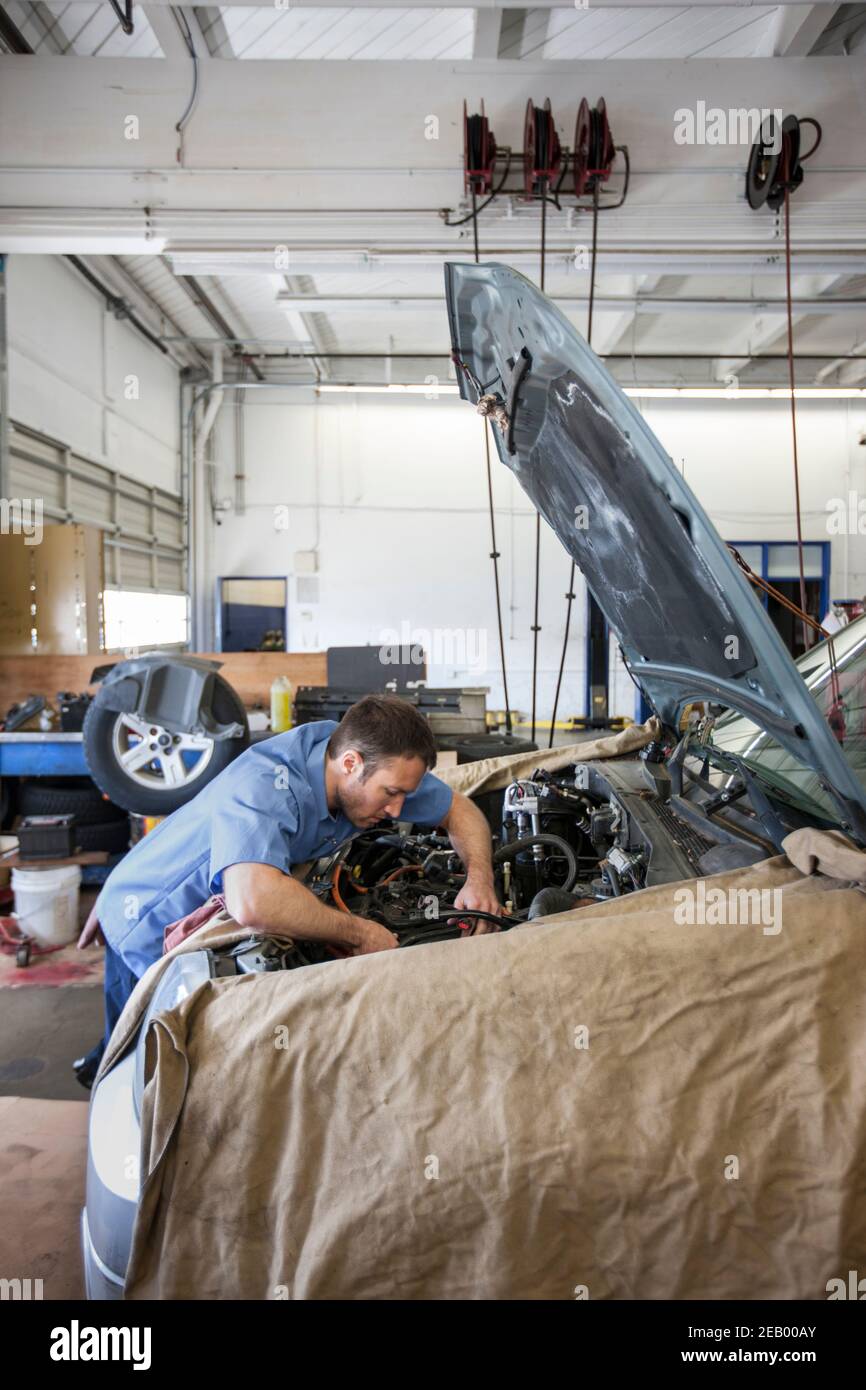 Mechaniker in der Autowerkstatt lehnt in den Motor des Autos Er arbeitet daran Stockfoto