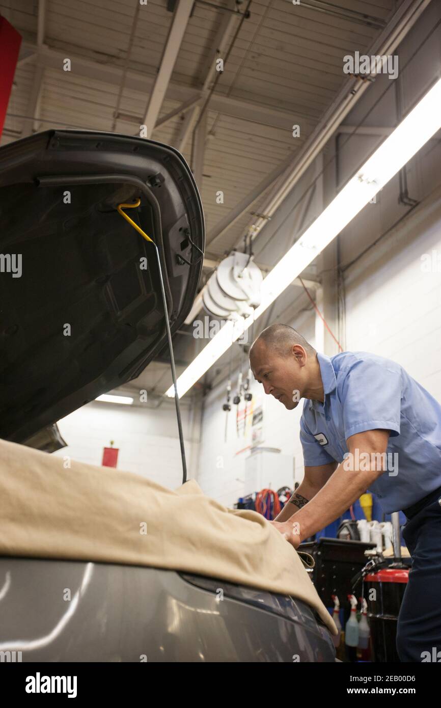 Der Mechaniker von Pacific Islander stützt sich bei seiner Arbeit auf ein Auto Im Motorraum in einer Autowerkstatt Stockfoto