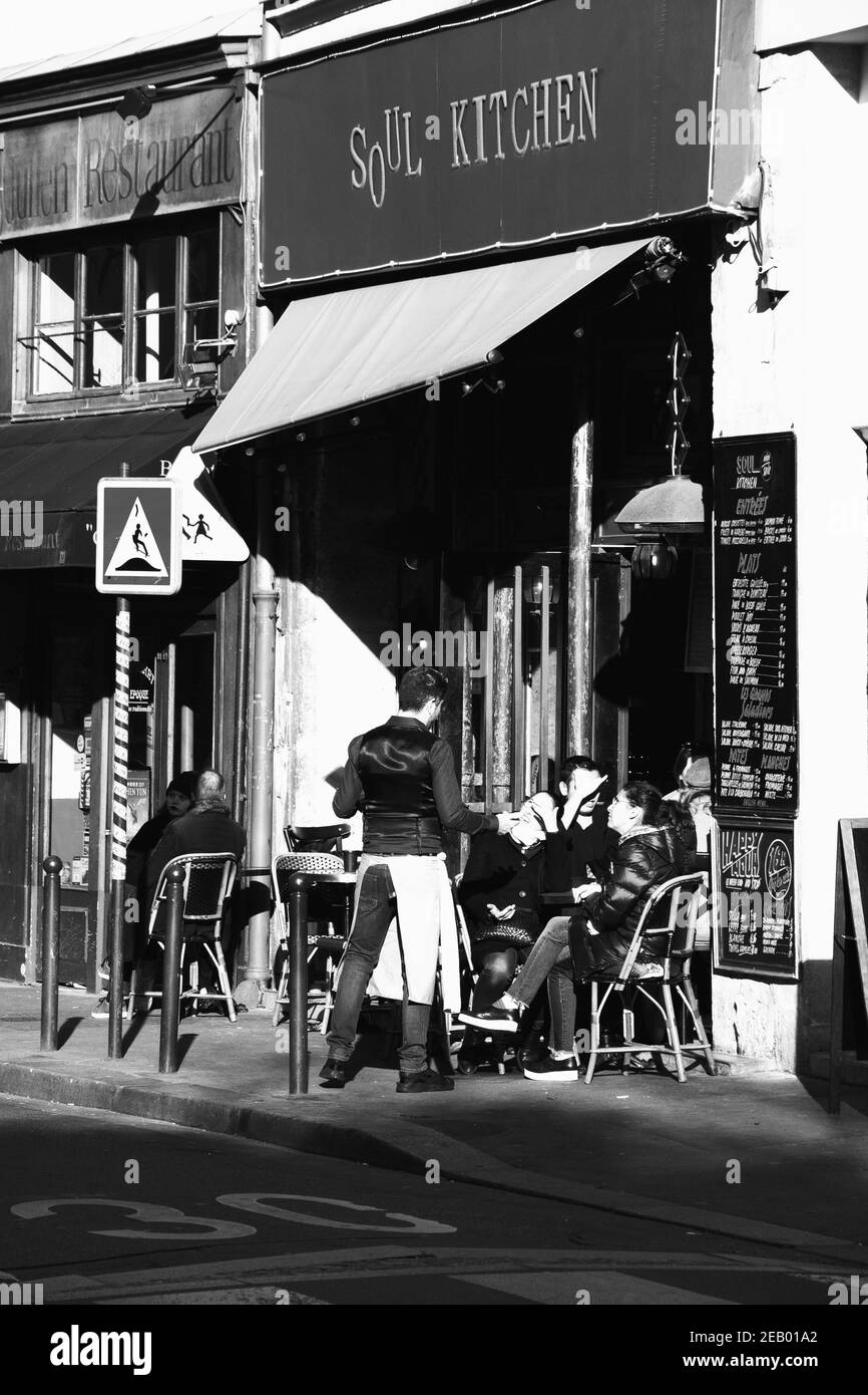 PARIS, FRANKREICH - 14. FEBRUAR 2019: Kellner, der Gäste auf der Terrasse des Soul Kitchen Cafés im Quartier Latin bedient; 30 km-Schild auf der Straße. Schwarz-weiß. Stockfoto