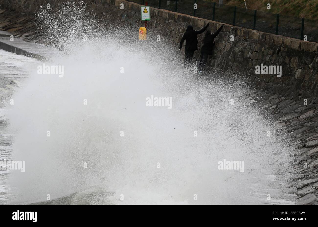 Zwei Mann erklimmen eine Wand, um zu vermeiden, dass die Wellen entlang der Küste am Seapoint Beach in Dublin brechen, da Met Eireann zwei Wetterwarnungen herausgegeben hat, darunter starke bis orkanartige Südostwinde in Verbindung mit Regen, Schnee und Schnee. Bilddatum: Donnerstag, 11. Februar 2021. Stockfoto