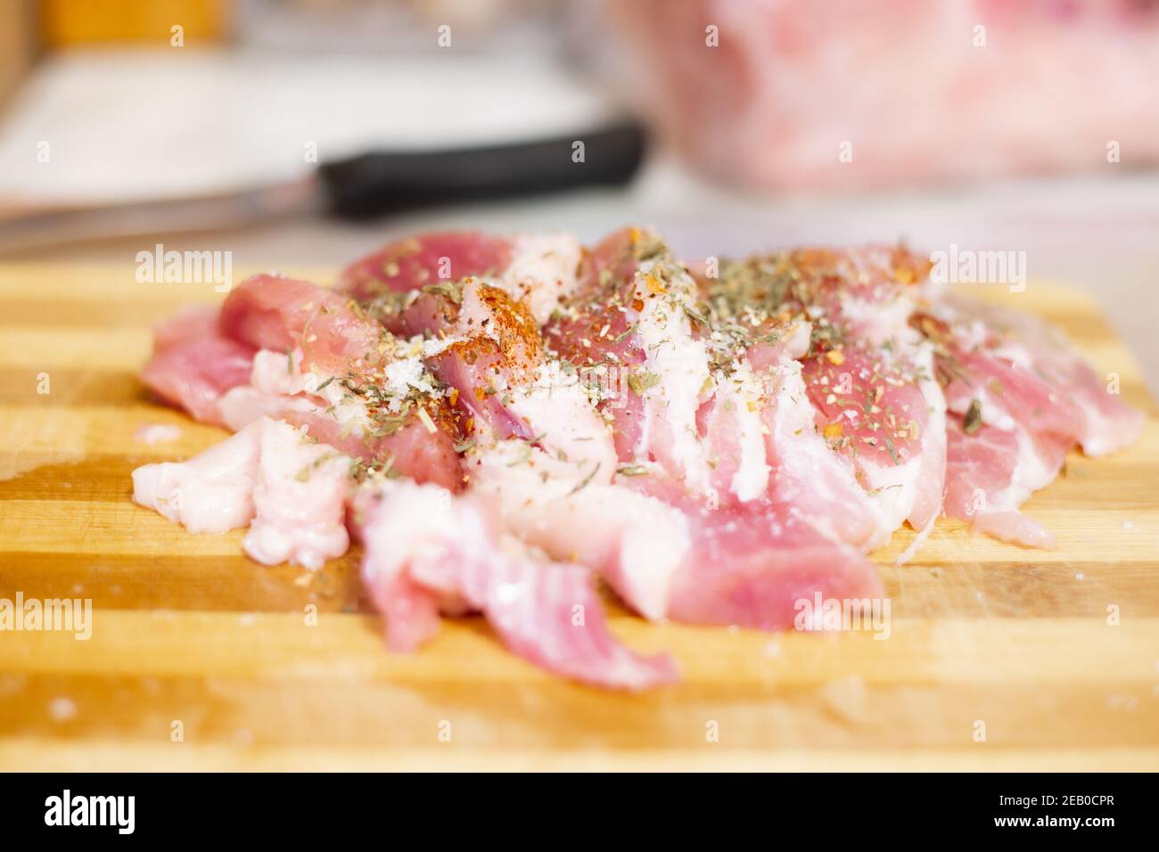 Rohes Schweinefleisch auf einem Holzbrett, bestreut mit Gewürzen, neben einem Messer, selektive Fokus Stockfoto