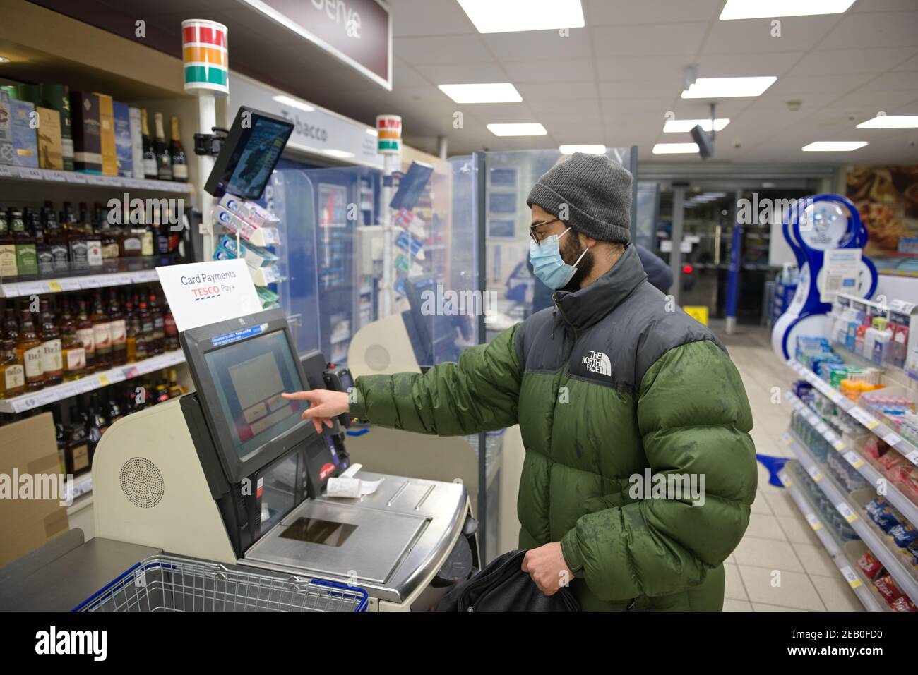 Sheffield, Großbritannien, 14th. Januar 2021: Ein junger Mann mit Gesichtsmaske und Winterkleidung zahlt an einem Tesco Express-Selbstbedienungskassen Lebensmittel Stockfoto
