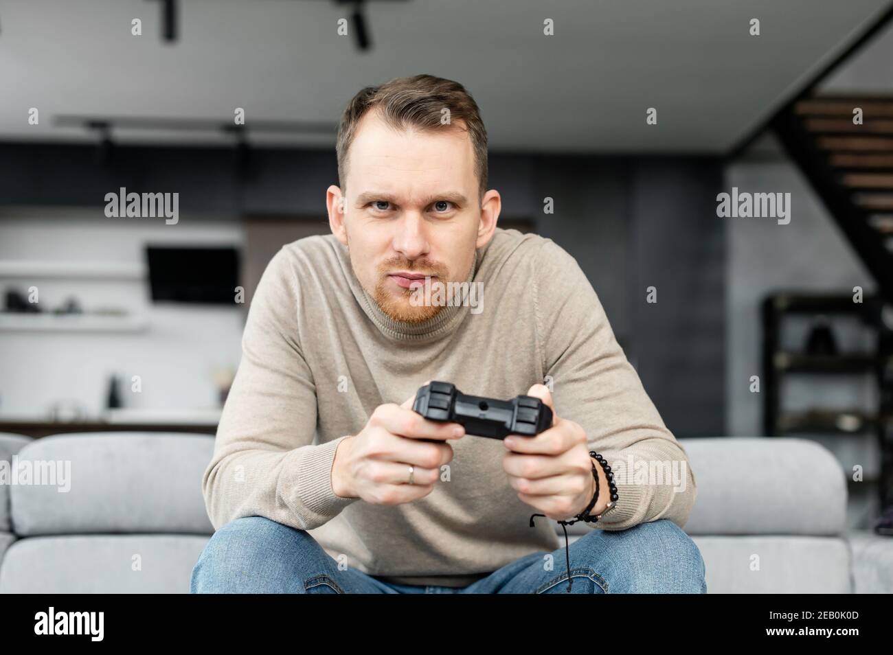 Gut aussehend aufgeregt jungen Kerl verbringt Freizeit spielen Videospiel, Glücksspiel Kerl mit einem Joystick sitzt auf der Couch, spielen auf der Konsole zu Hause Stockfoto Gut aussehend aufgeregt jungen Kerl verbringt Freizeit spielen Videospiel, Glücksspiel Kerl mit einem Joystick sitzt auf der Couch, spielen auf der Konsole zu Hause Stockfoto