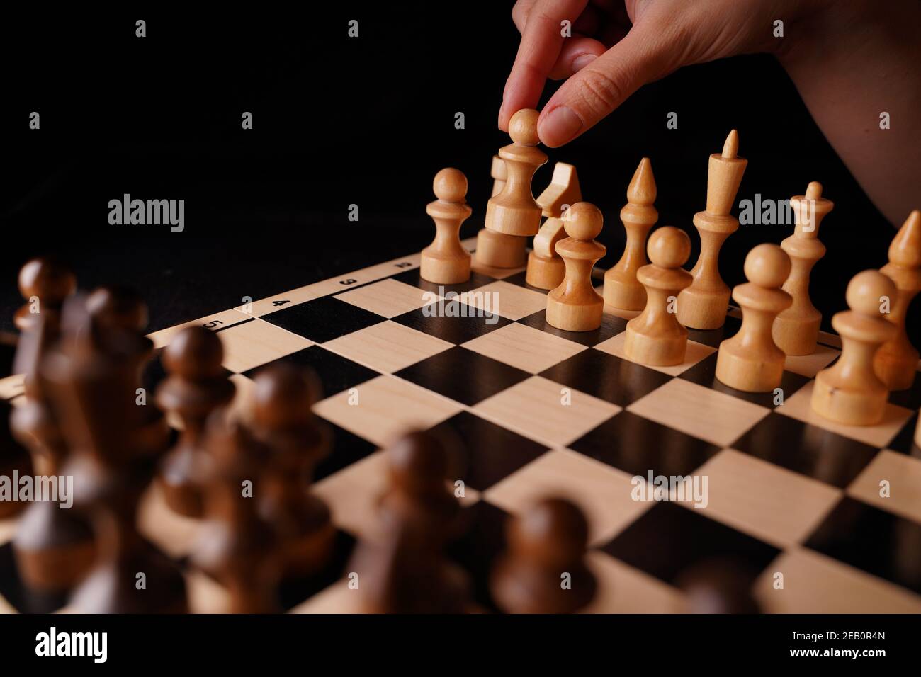 Nahaufnahme von weißen und schwarzen Schachfiguren aus Holz an Bord. Die Hand der Frau macht den ersten Zug der weißen Spielfigur auf dem Schachbrett. Konzept des intelligenten, logischen A Stockfoto