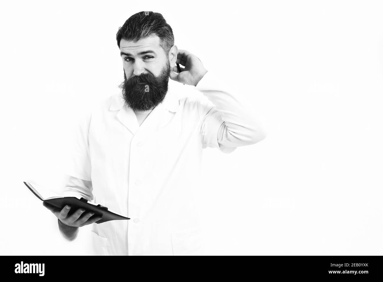 Postgraduate Student hält Notebook mit Stift in medizinischen Kleid isoliert auf weißem Studio Hintergrund. Medizinkonzept. Bärtiger Mann, langer Bart. Brutaler kaukasischer Arzt oder unrasierte Hipster, Stockfoto