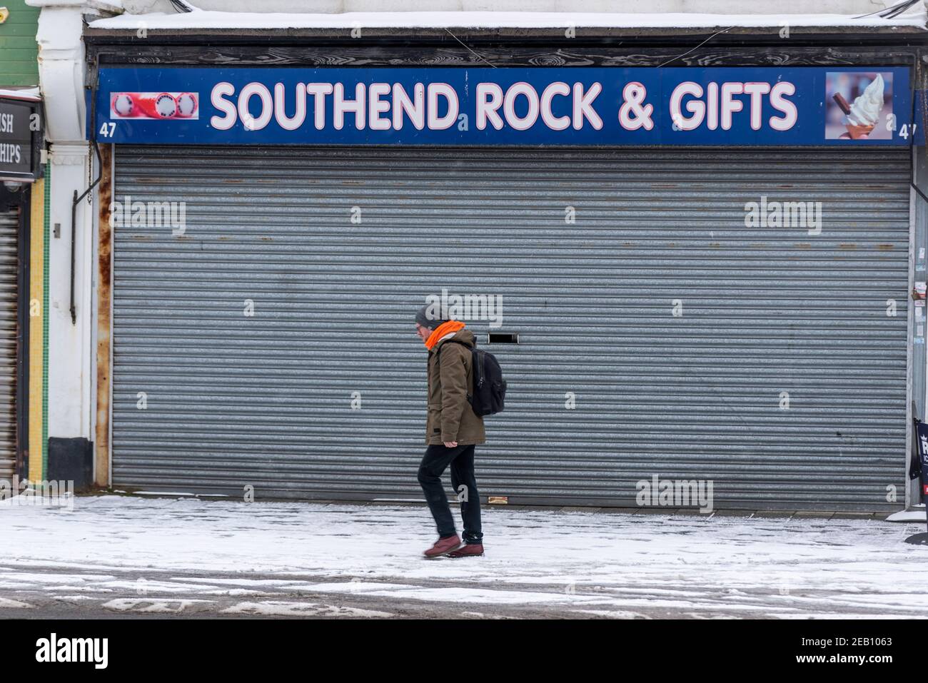 Person, die an einem geschlossenen Souvenirladen in Southend on Sea, Essex, Großbritannien, mit Schnee von Storm Darcy vorbeiläuft. Küstenstadt im Winter. Business Economy direkt am Meer Stockfoto