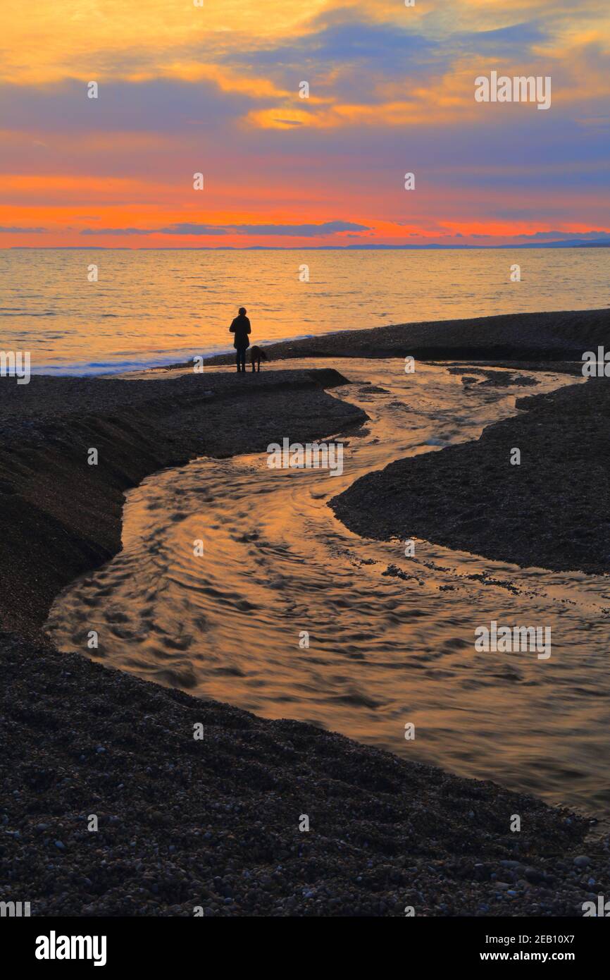 Silhouette eines Mannes, der am Strand bei Sonnenuntergang spazierengeht Stockfoto