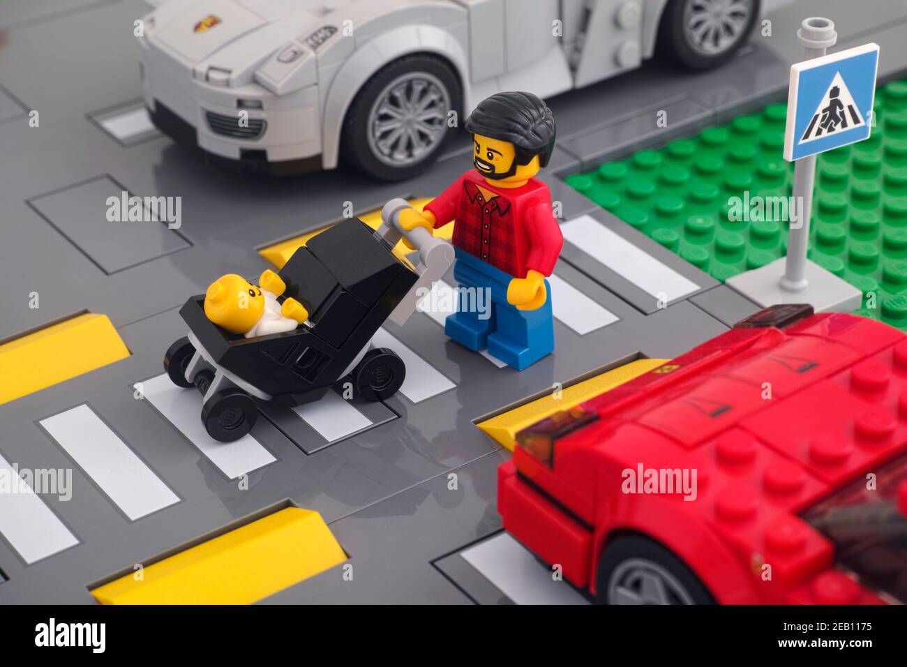 Tambov, Russische Föderation - 07. Februar 2021 Lego minifigur, die einen Kinderwagen mit einem Baby in ihm über die Straße mit einem Fußgänger schieben Stockfoto