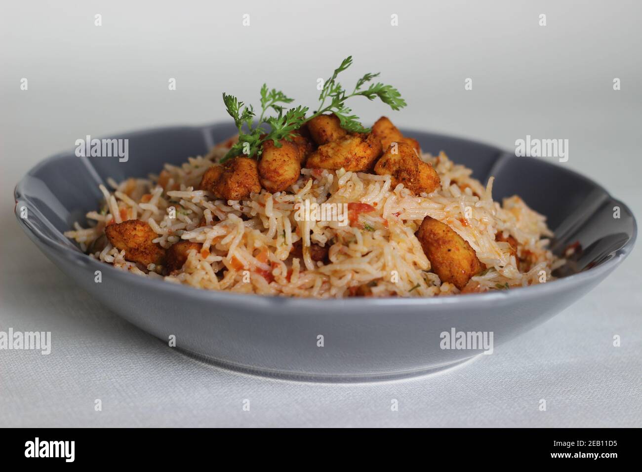 Tomatenreis serviert mit Raita und gebratenen Hähnchenbissen ohne Knochen. Aufnahme auf weißem Hintergrund. Serviert auf einer grauen Schüssel Stockfoto