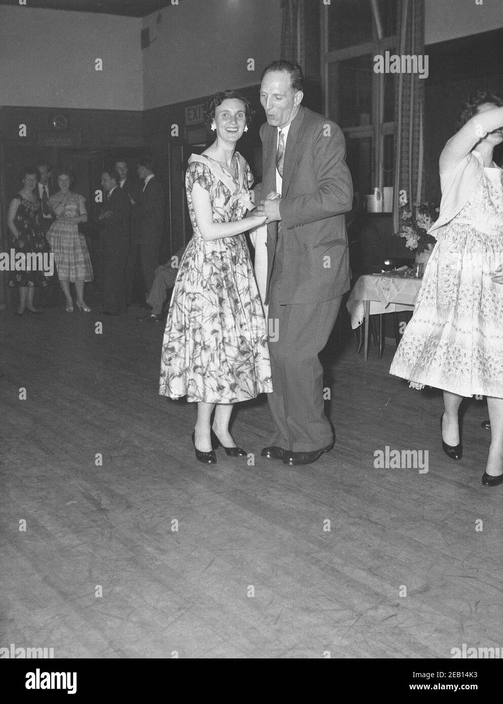 1950s, historisch, ein Mann und eine Dame tanzen zusammen auf einer Party auf einem Holzboden in einem Veranstaltungsraum in einem Hotel, England, Großbritannien. Der Mann trägt einen Anzug und Krawatte und die Dame ein langes Kleid mit Blumenmuster, das an die weibliche Mode der Zeit anmutet. Musikalisch war es die Zeit des Swings, der Big Band und des Skiffles, des Vorläufers zum Rock and Roll. Stockfoto