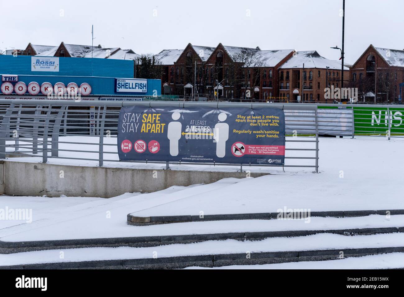 Marine Parade in Southend on Sea, Essex, Großbritannien, mit Schnee von Storm Darcy. COVID 19 sicher bleiben, auseinander bleiben, soziale Distanzierungsbanner. Steinfront Stockfoto