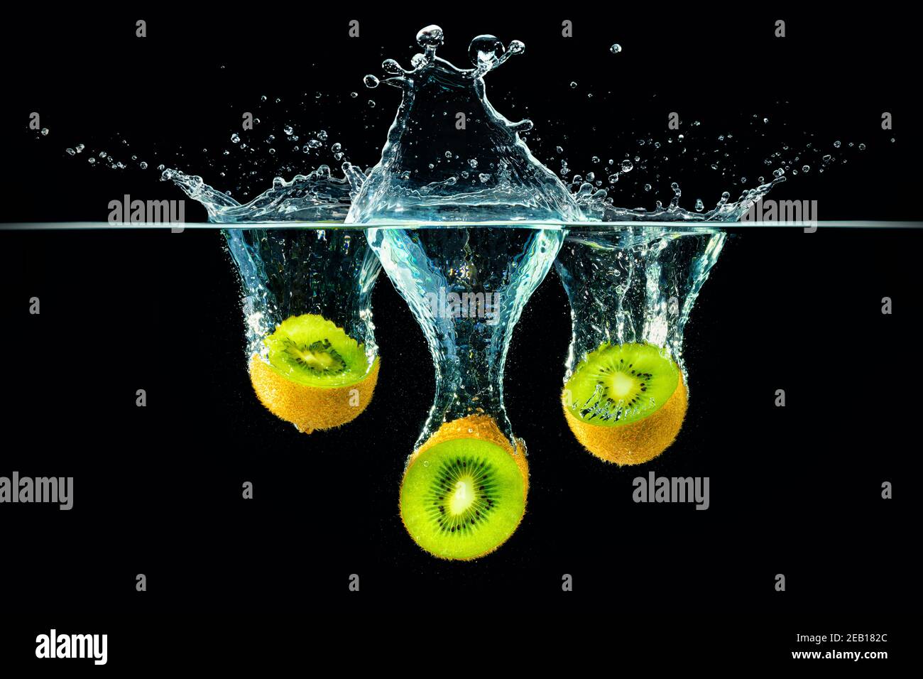 Frische Kiwi-Scheiben fallen in Spritzwasser Stockfoto