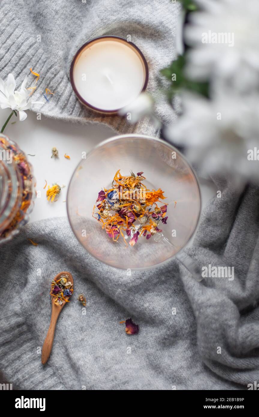 Eine transparente Tasse mit trockenem Blumentee und einem Holzbecher Löffel auf einem Pullover Stockfoto