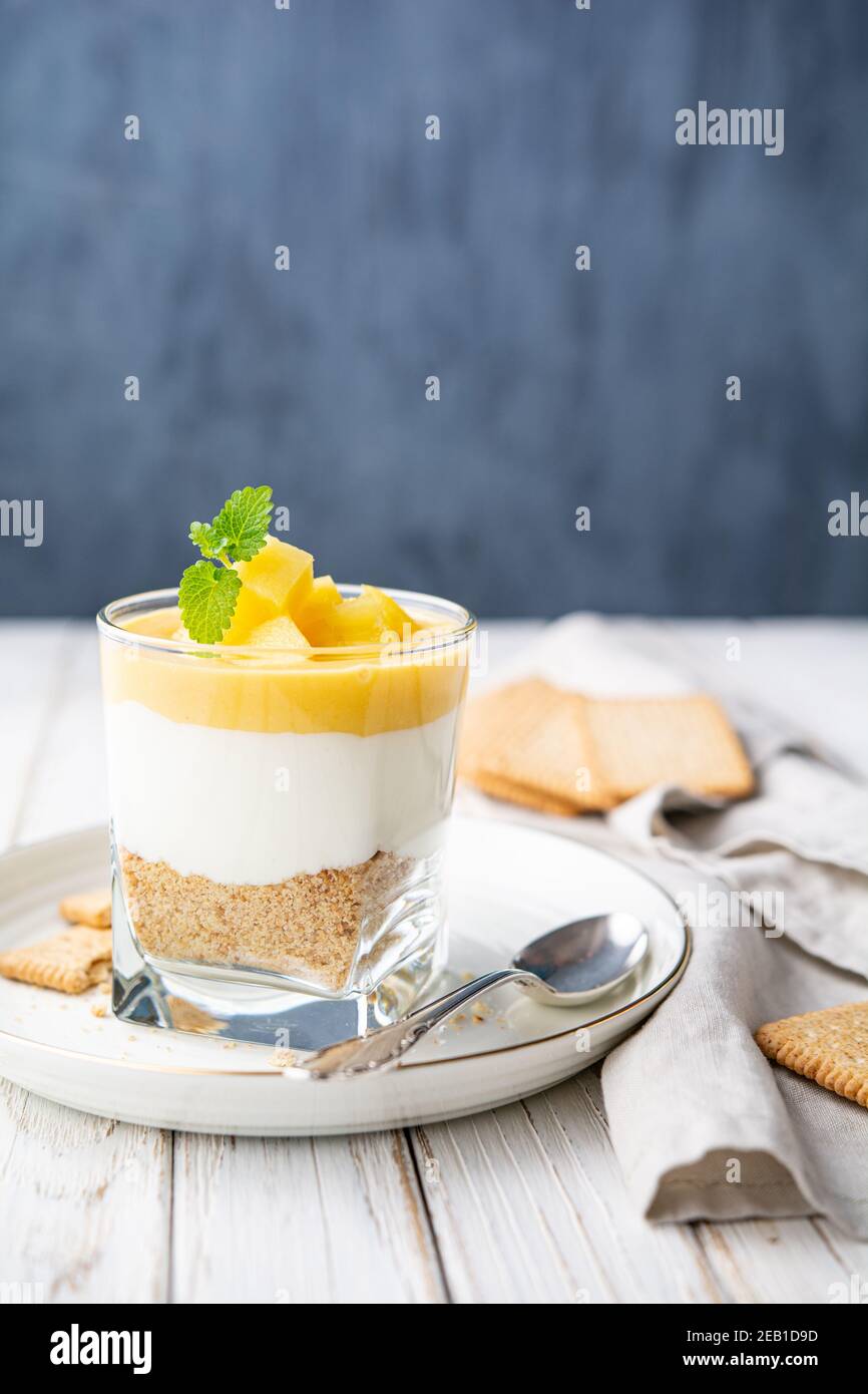 Süßes mehrlagiges Dessert mit zerkleinerten graham Crackers, Frischkäse und Ananasgebäck, garniert mit frischen Fruchtscheiben in einem Glas auf altem Holzbackg Stockfoto