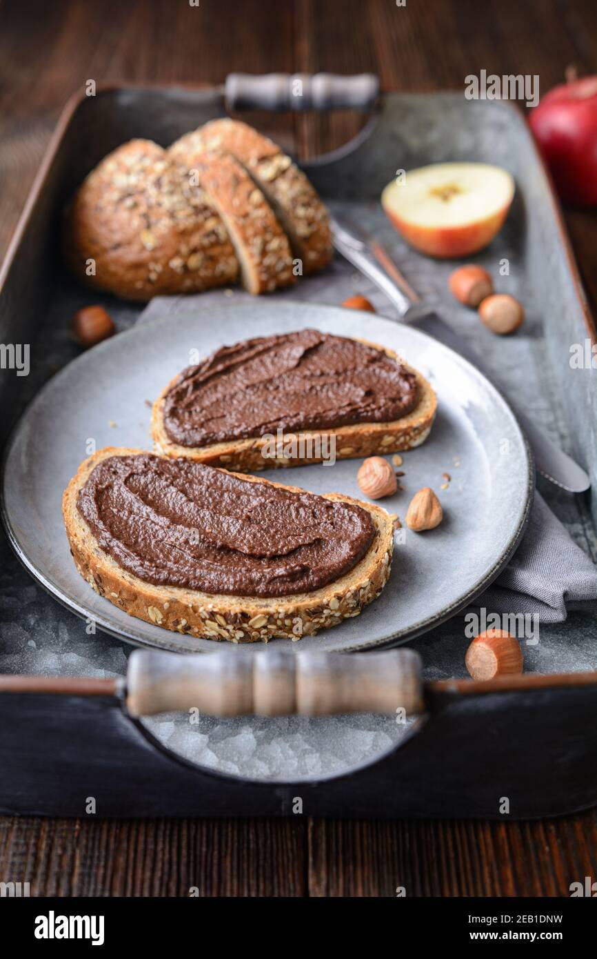 Gesundes Frühstück, Scheiben Vollkornbrot mit Apfelaufstrich aus Kakaopulver, geröstete gemahlene Haselnüsse und dunkle Schokolade auf rustikalem Holz Stockfoto