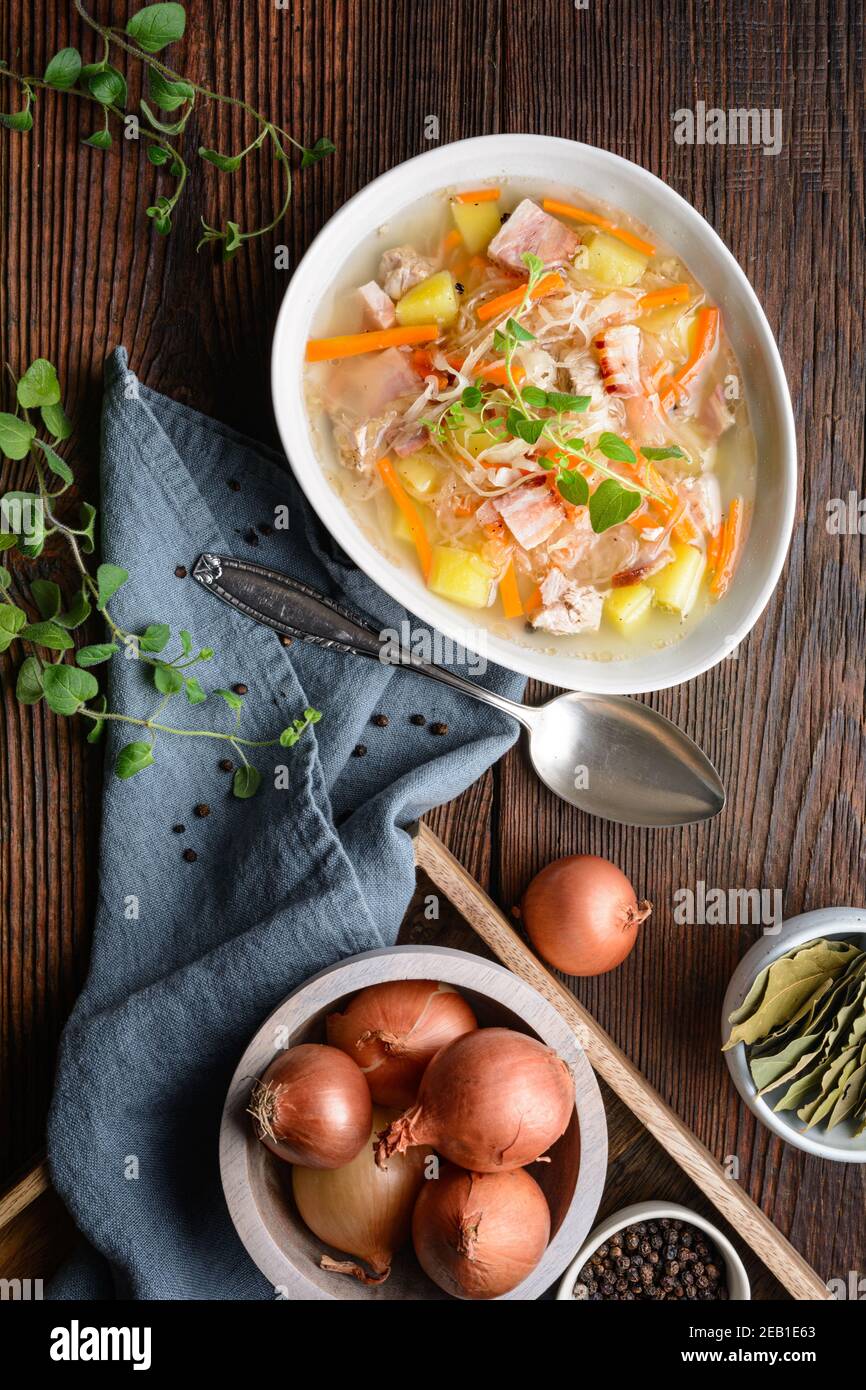 Kapusniak, klassische polnische Suppe aus Sauerkraut, Schweinebrippen, geräuchertem Speck, Kartoffeln, Karotten und anderem Gemüse in tiefer Keramikplatte auf rustikalem Holz Stockfoto