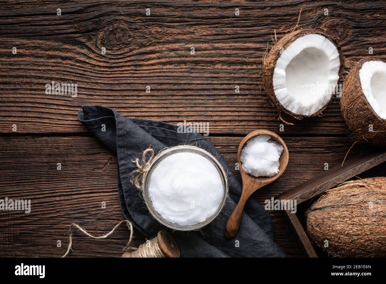 Superfood kaltgepresstes Bio-Kokosöl in einem Glas, mit frischer Nuss auf rustikalem Holzhintergrund mit Kopierraum dekoriert Stockfoto