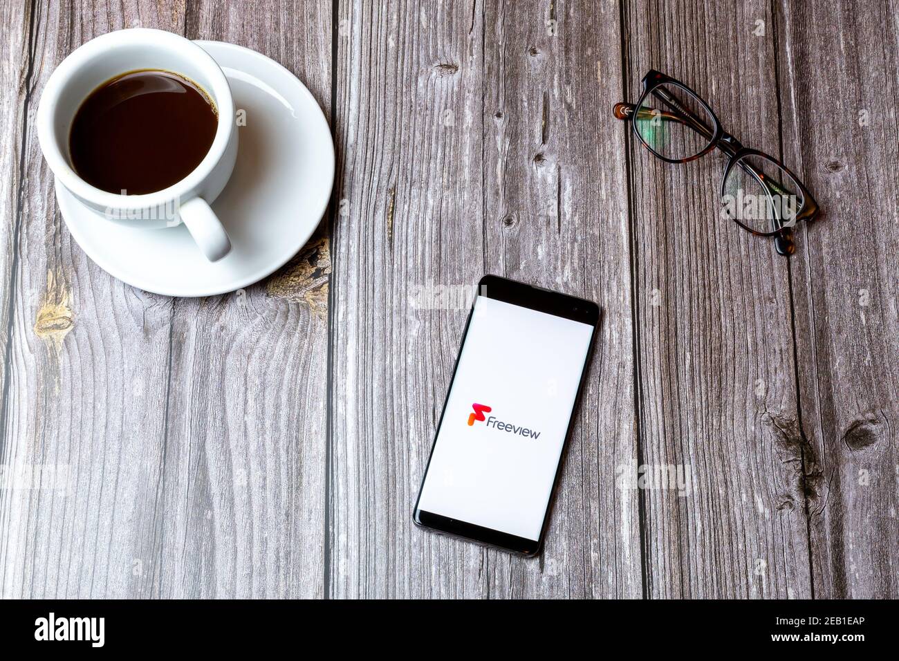 Ein Handy oder Handy auf einem Holz gelegt Tabelle mit der Freeview TV App auf dem Bildschirm als nächstes geöffnet Zu einem Kaffee Stockfoto