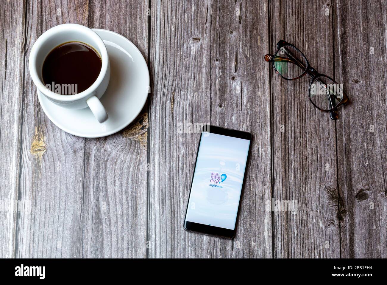Ein Handy oder Handy auf einem Holz gelegt Tabelle mit der Anglian Wasser-App auf dem Bildschirm als nächstes geöffnet Zu einem Kaffee Stockfoto