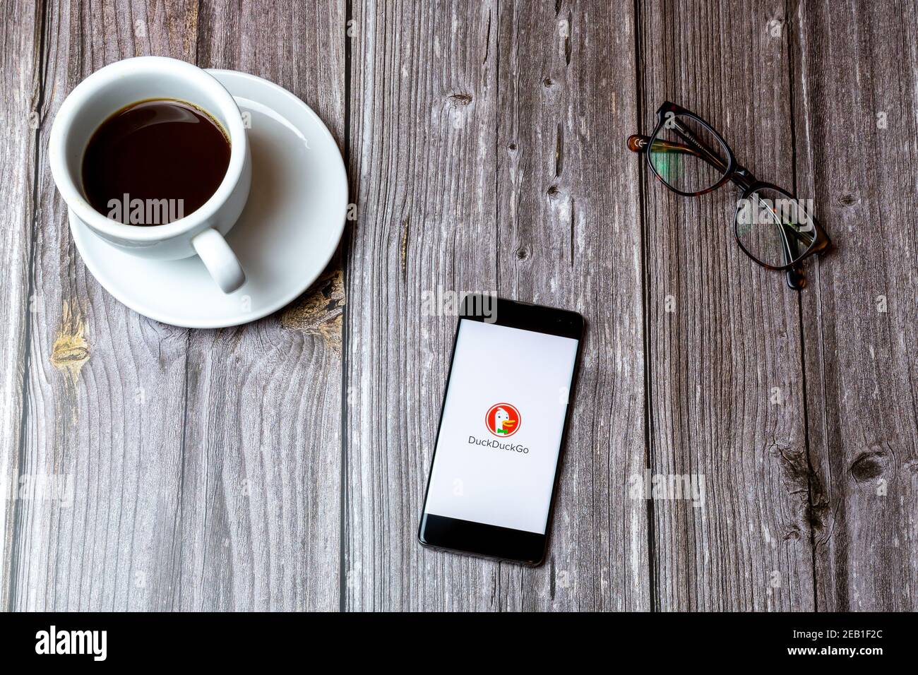Ein Handy oder Handy auf einem Holz gelegt Tabelle mit der DuckDuckGo App auf dem Bildschirm neben geöffnet Ein Kaffee Stockfoto