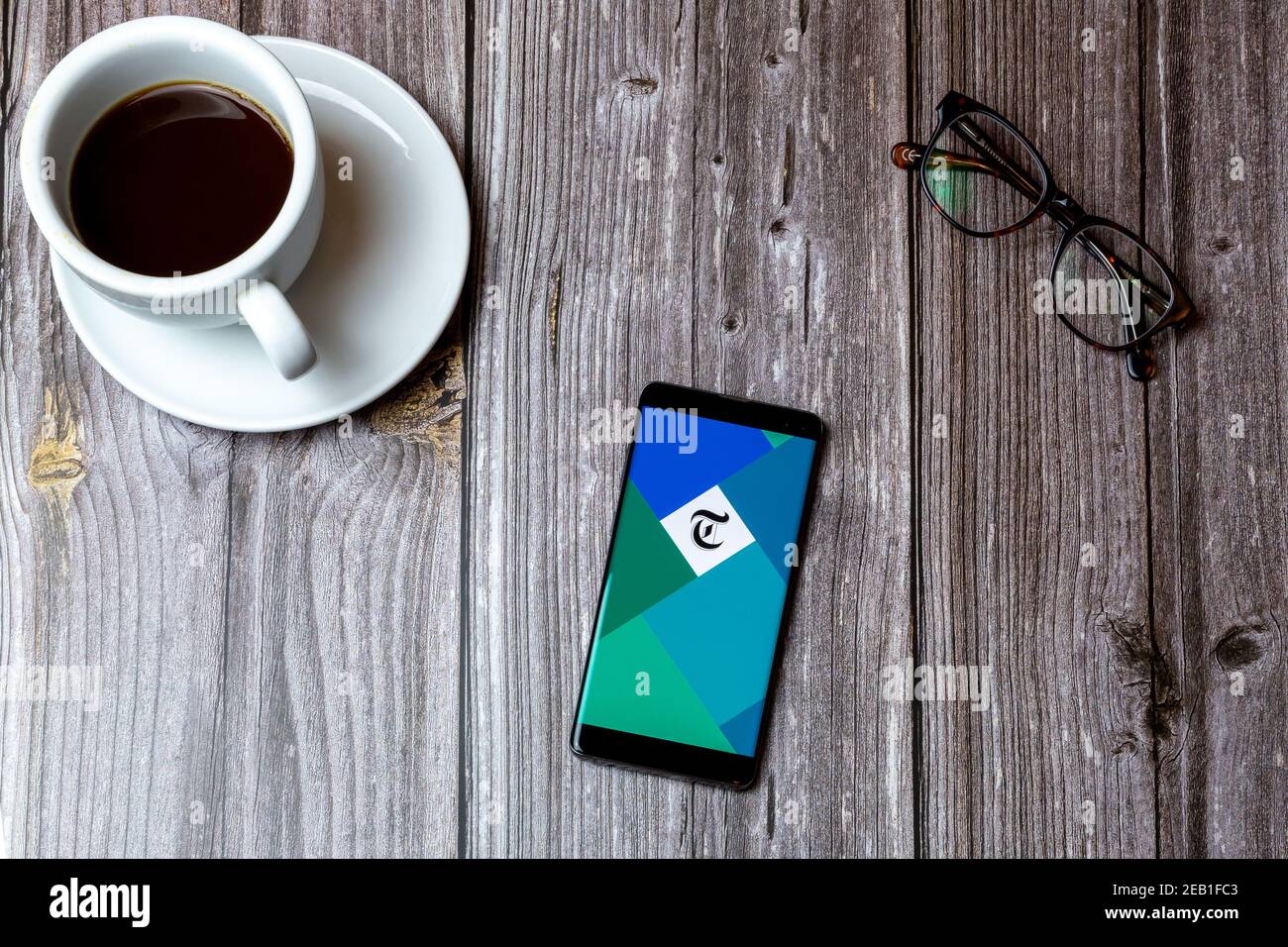 Ein Handy oder Handy auf einem Holz gelegt Tabelle mit der Telegraph Zeitung App auf dem Bildschirm als nächstes geöffnet Zu einem Kaffee Stockfoto