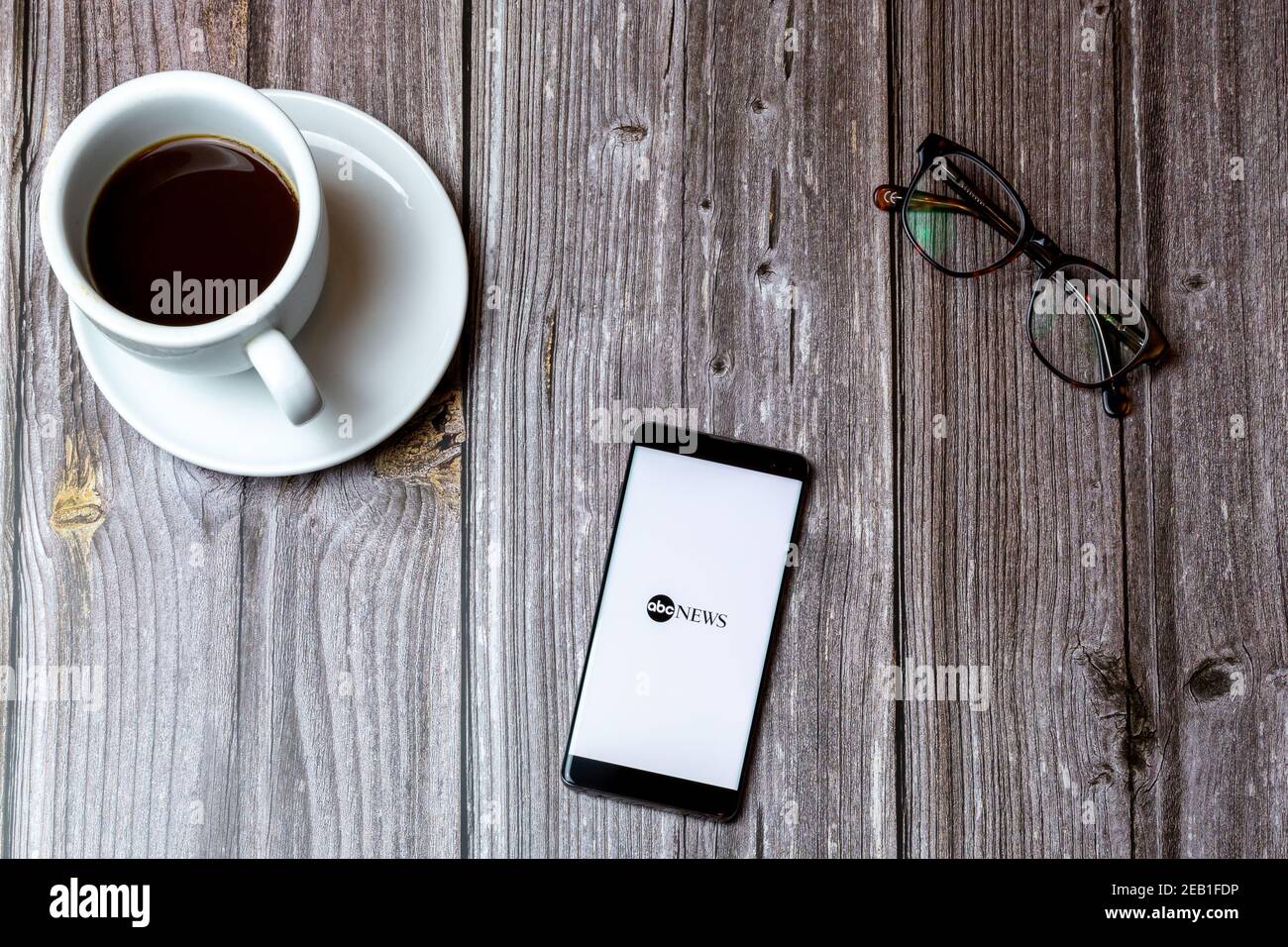 Ein Handy oder Handy auf einem Holz gelegt Tabelle mit der ABC News App auf dem Bildschirm als nächstes geöffnet Zu einem Kaffee Stockfoto