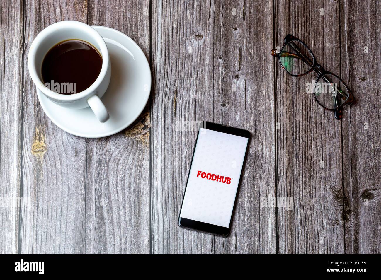 Ein Handy oder Handy auf einem Holz gelegt Tabelle mit geöffneter foodHub-App auf dem Bildschirm neben Ein Kaffee Stockfoto