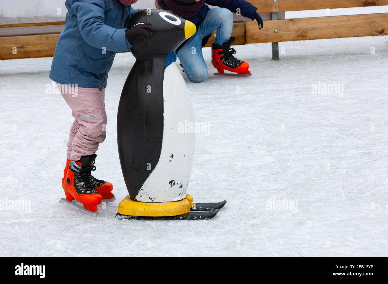 Kinder Schlittschuh mit Pinguin Skating Hilfe auf Eisbahn betrieben für  Kinder Erholung während der Winterferien. Beine in orange Schlittschuhe.  Weihnachtsurlaub Spaß Stockfotografie - Alamy