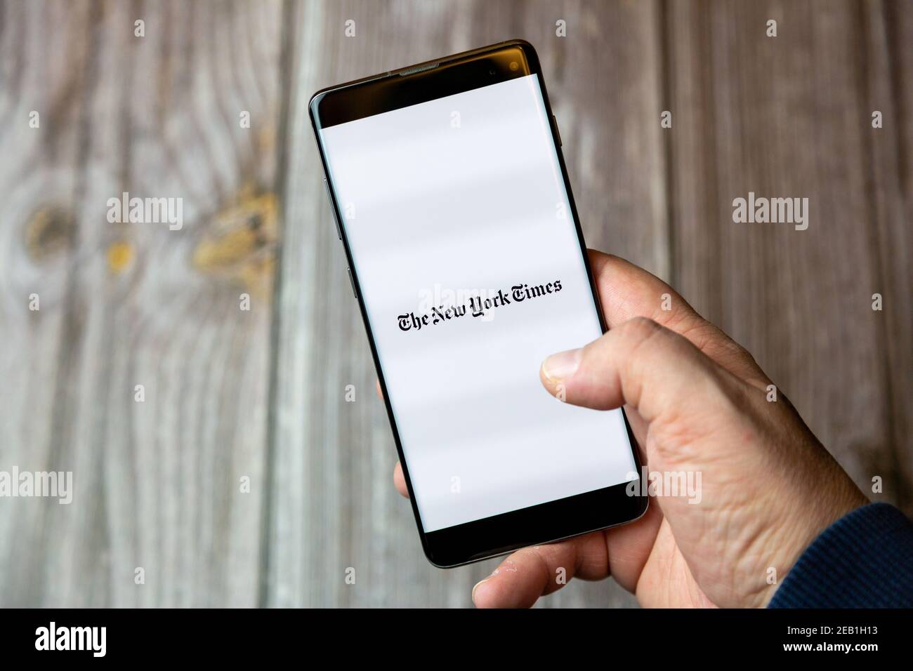 Ein Mobiltelefon oder Mobiltelefon, das von einem gehalten wird Hand mit der New York Times App geöffnet auf dem Bildschirm Stockfoto