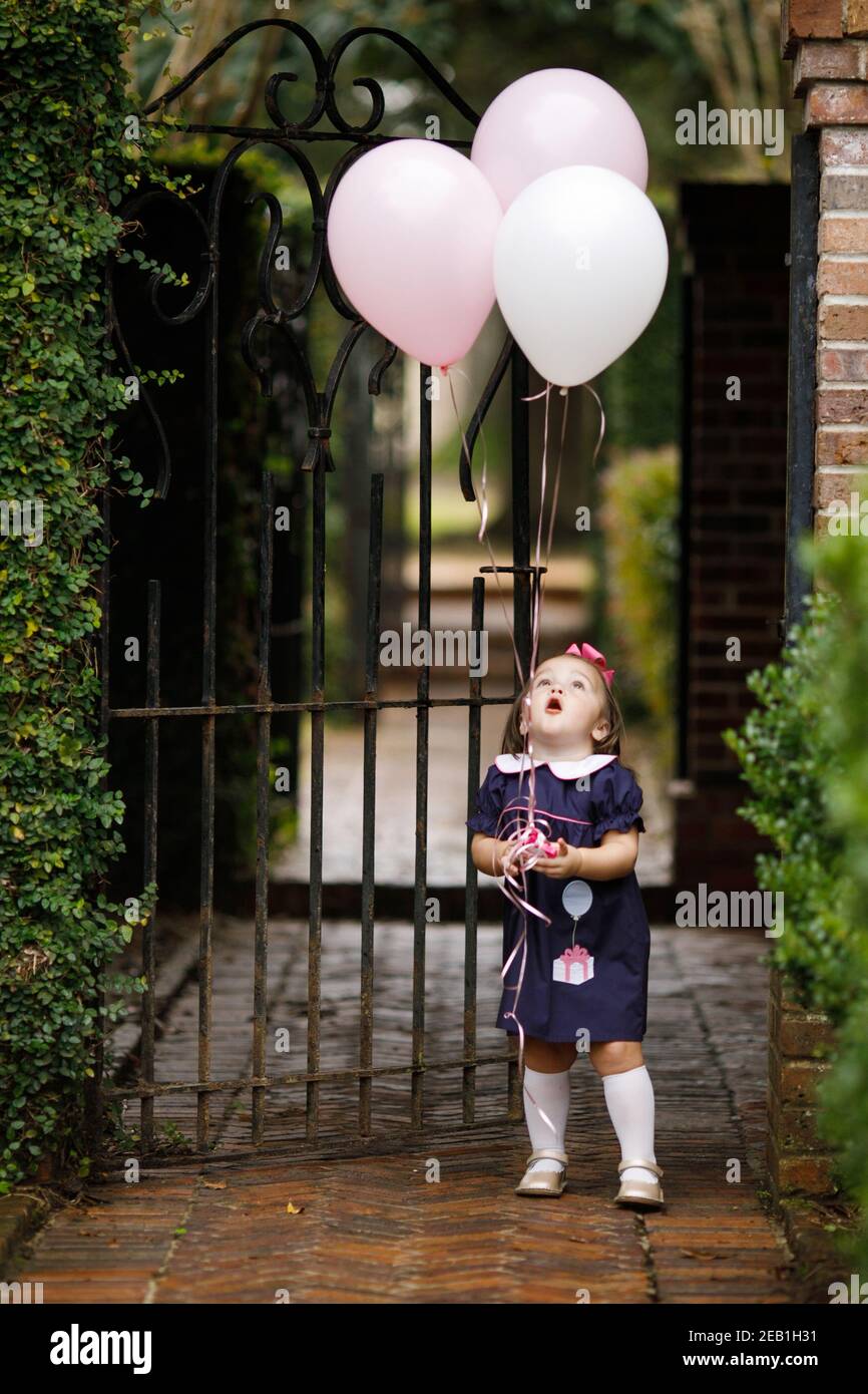 Kleines Kleinkind Mädchen mit rosa Geburtstag Ballons außerhalb in der Nähe eines Eisenzaun Stockfoto