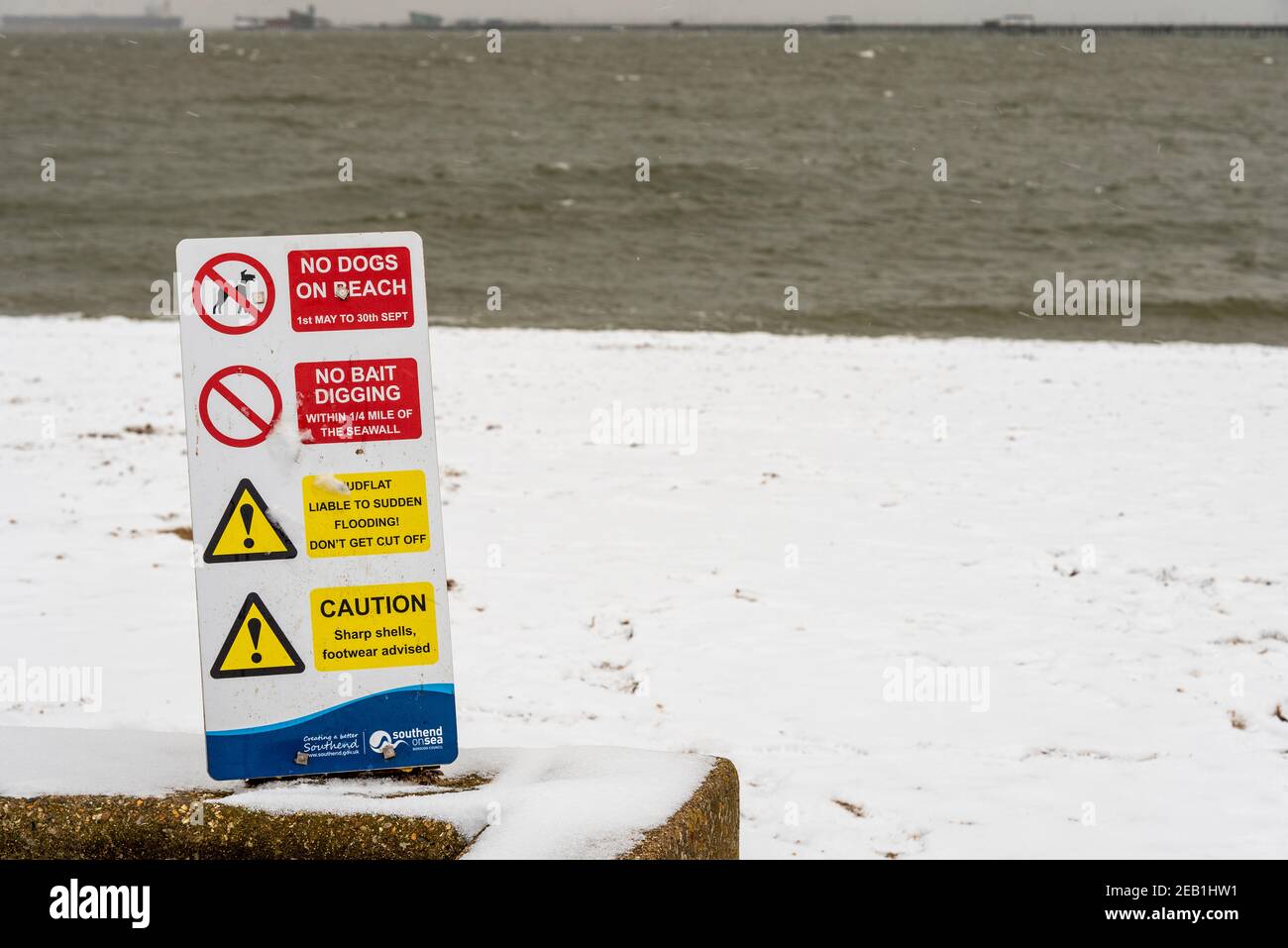 Strand Warnschild in Southend on Sea, Essex, UK, mit Schnee von Storm Darcy. Raue Themse Mündung und Pier dahinter. Keine Hunde am Strand, keine Köder graben Stockfoto